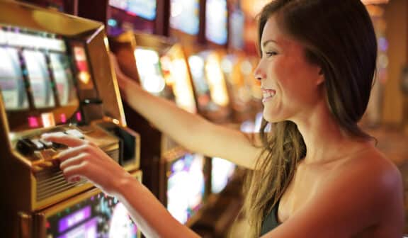 Asian woman gambling in casino playing on slot machines spending money. Gambler addict to spin machine. Asian girl player, nightlife lifestyle. Las Vegas, USA.